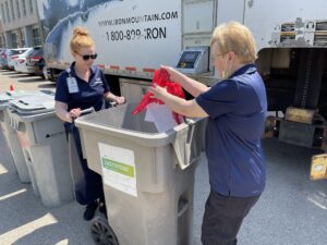 Two women dumping items in a trash can