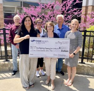 Four women outside holding a big check