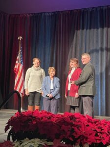 Four people on stage by a flag