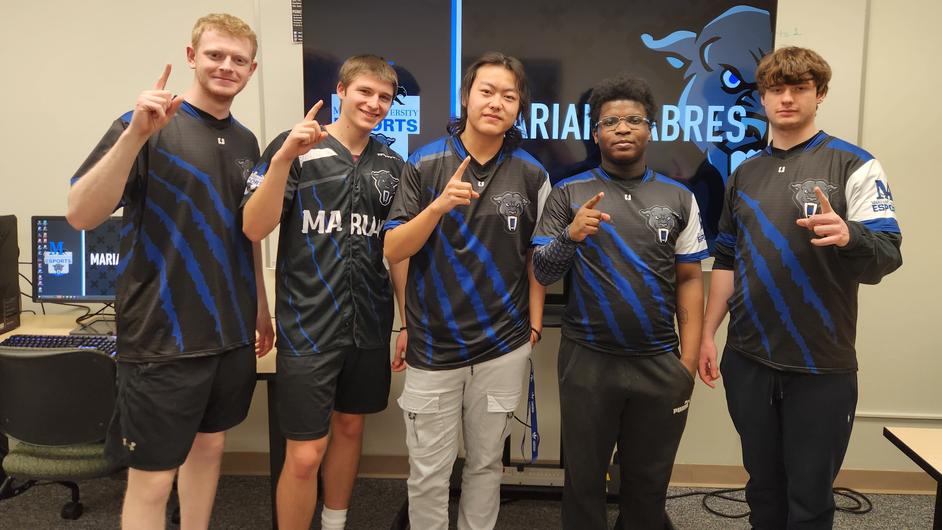 Five college students standing in front of computers.