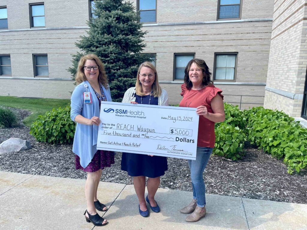 Three women outside holding a big check