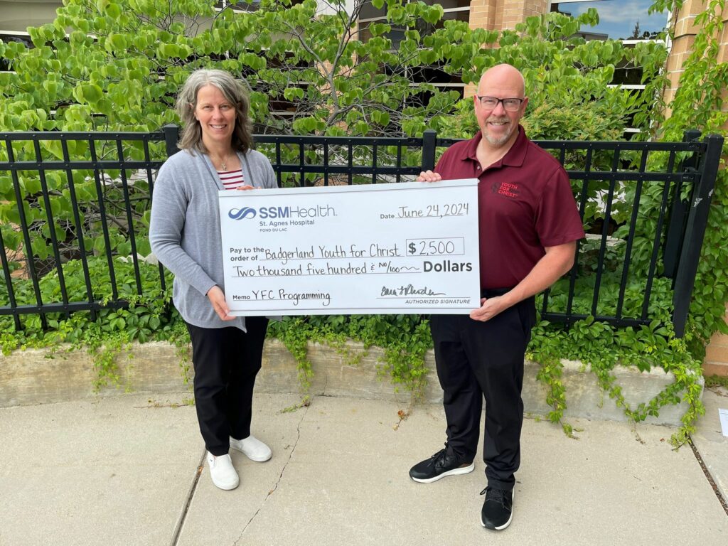 Two people outside holding a big check