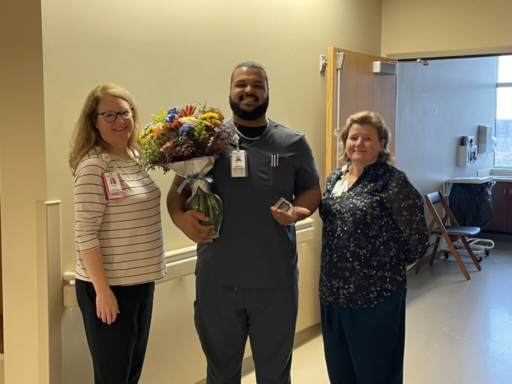 3 people in a hall with one holding flowers