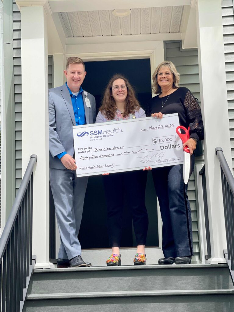 Three people standing on some steps with a big check