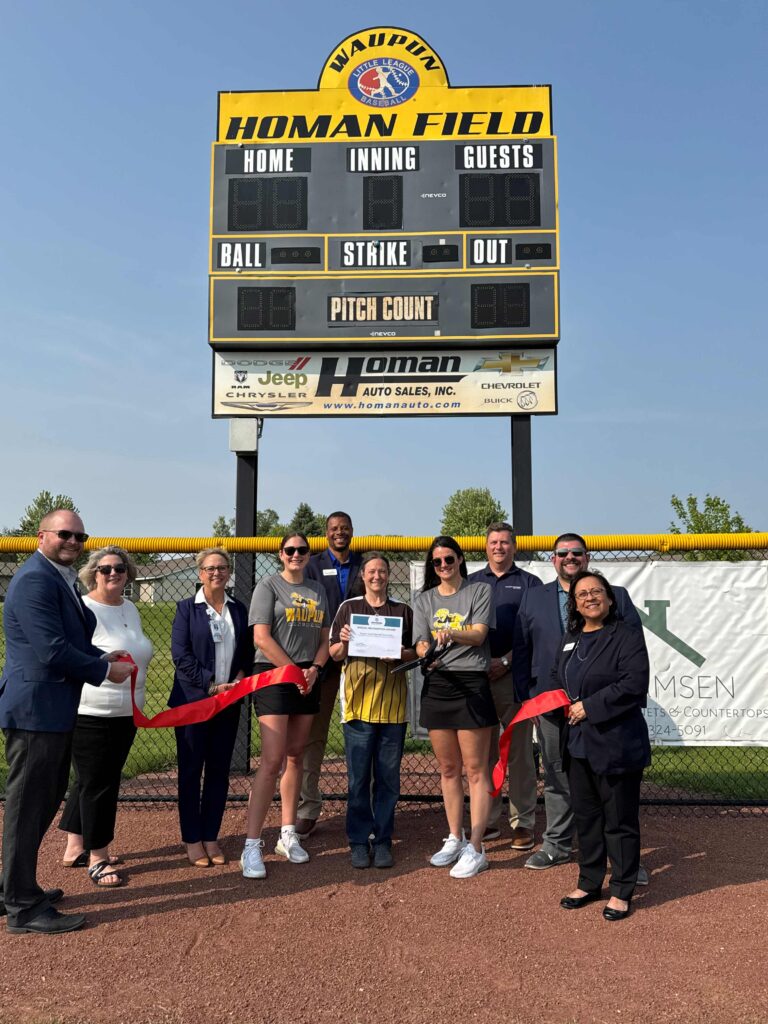 A group outside on a baseball field for a ribbon cutting
