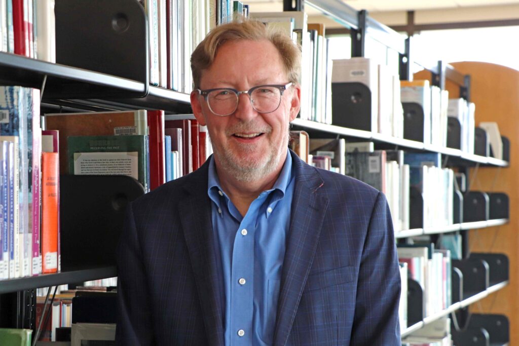 An older man standing next to bookshelves
