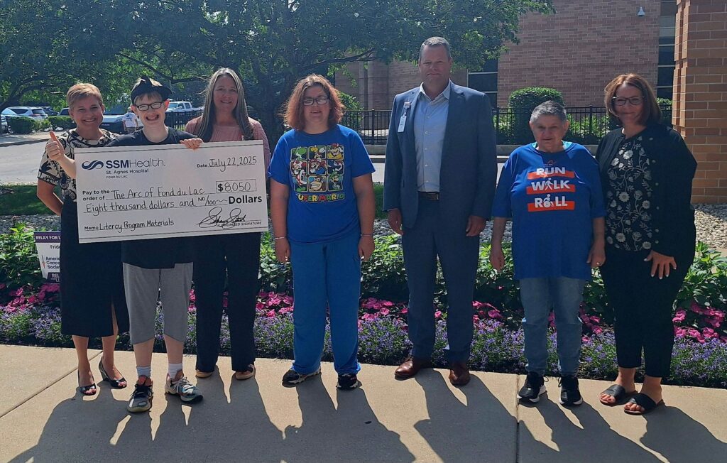 A group of six people outside with a big check