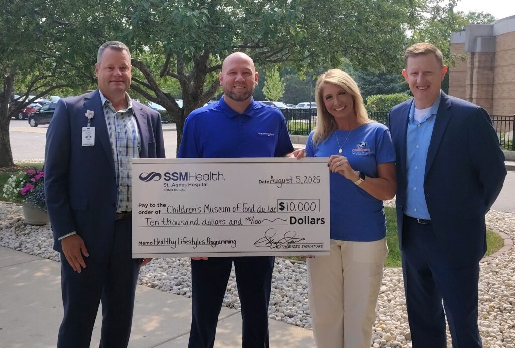 Four people outside holding a big check