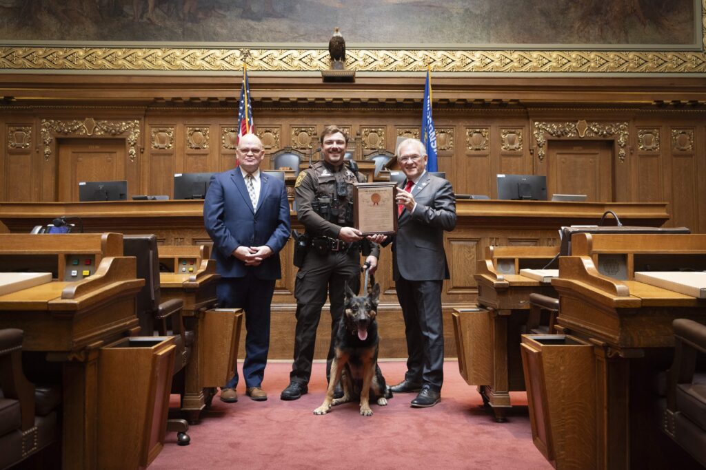 Three men with a dog and an award
