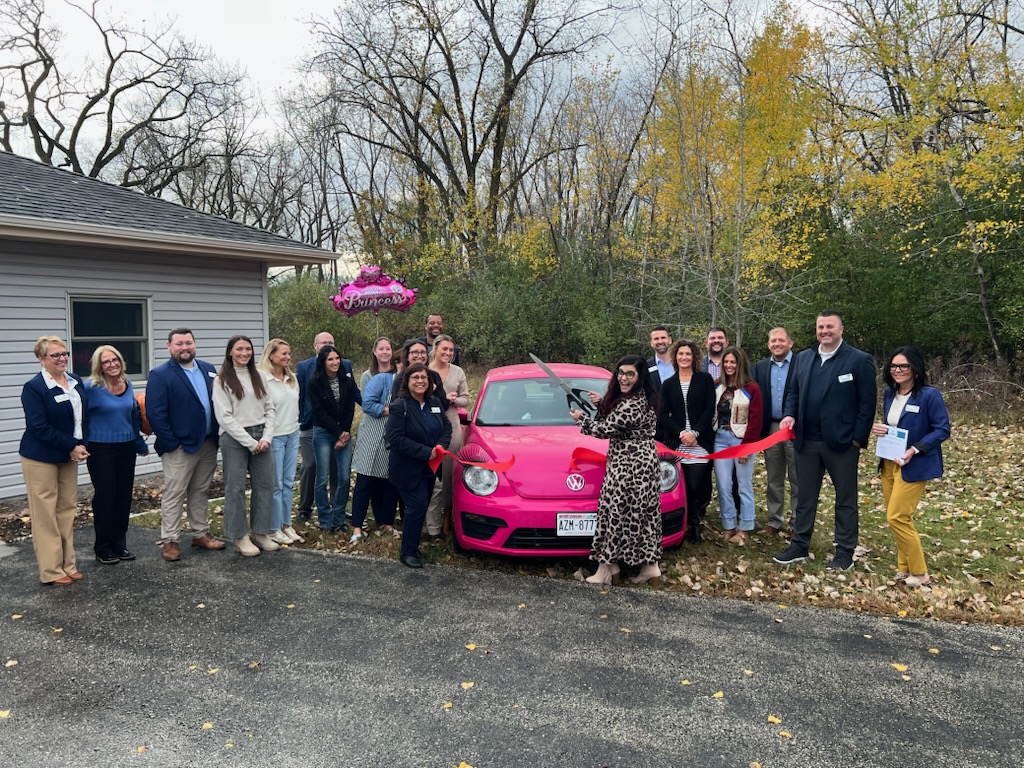 A large crowd outside for a ribbon cutting in front of a pink car