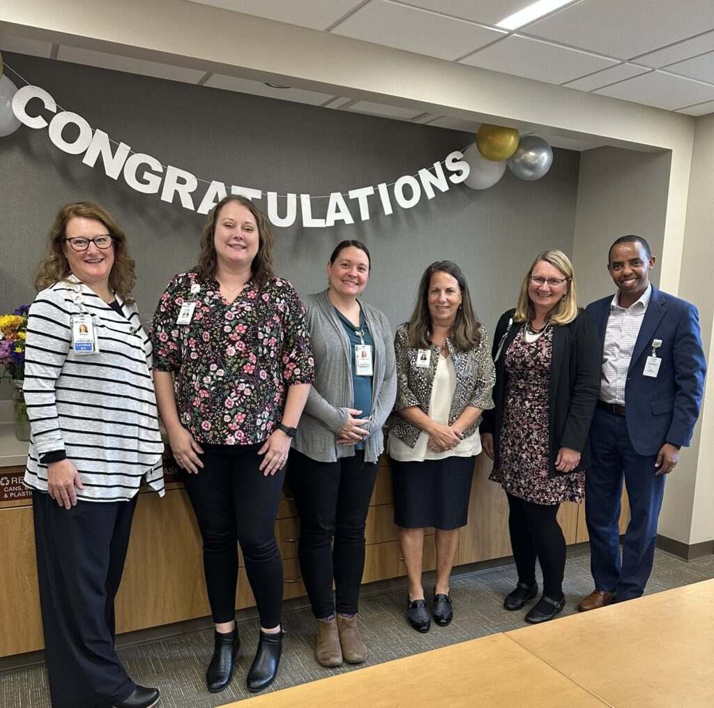 Six people standing under a congratulations sign