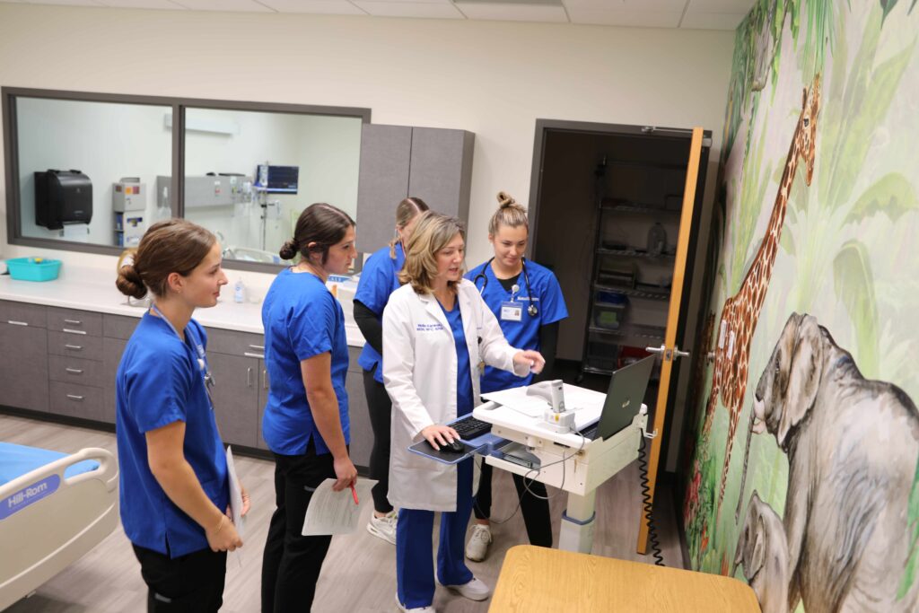 Four nursing students and a nursing instructor standing at a computer