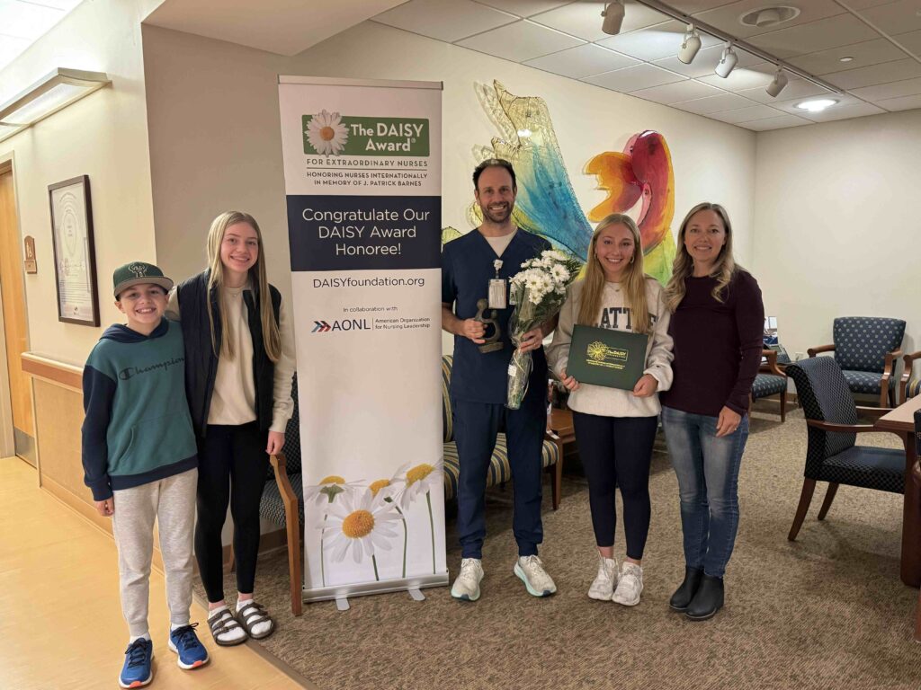 A man and his family standing by a sign holding flowers