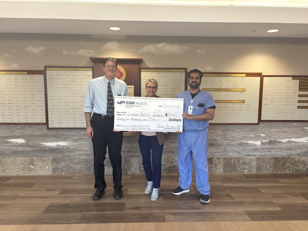 Three people standing in a hallway holding a big check