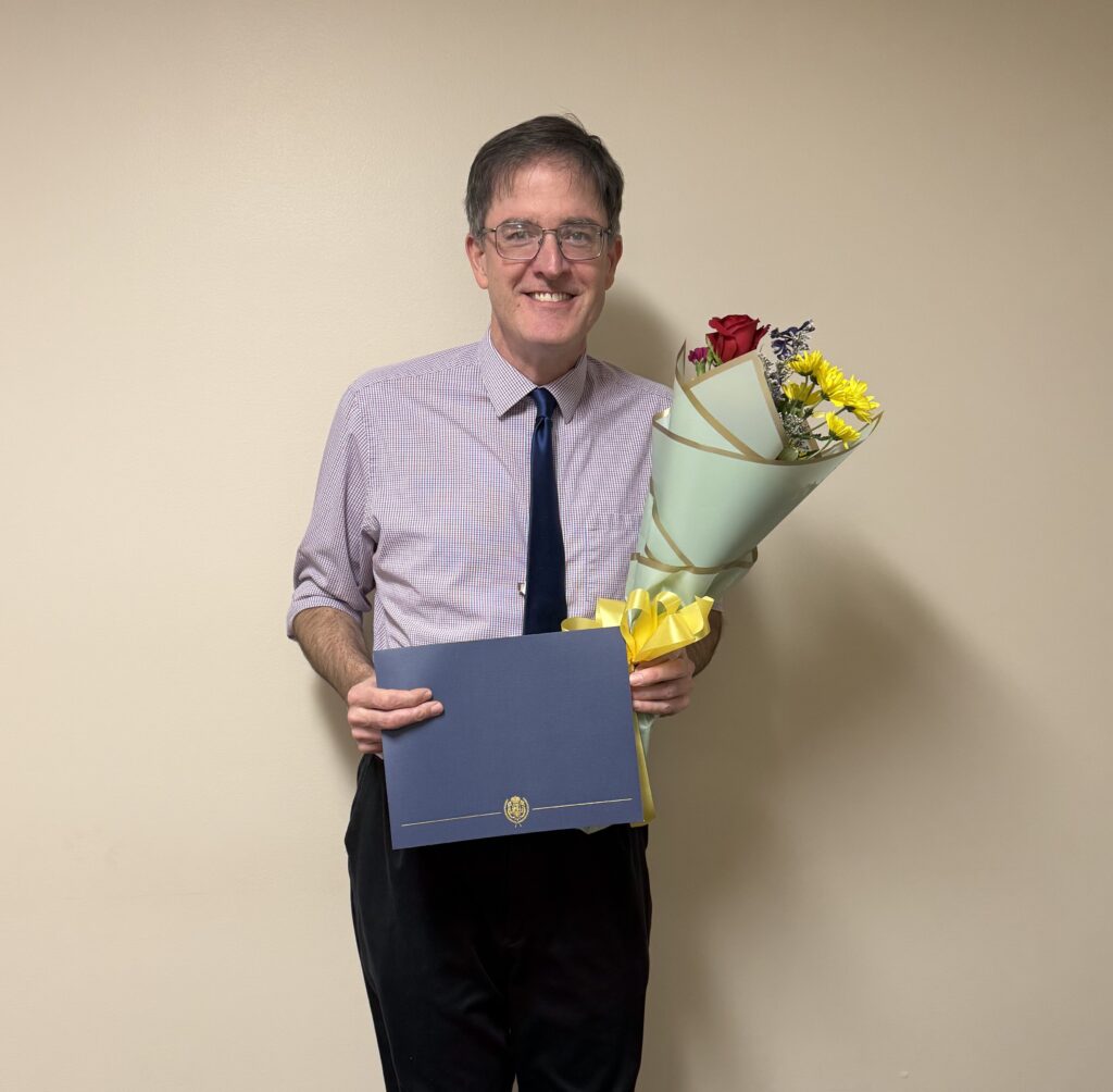 A man standing holding flowers and a certificate