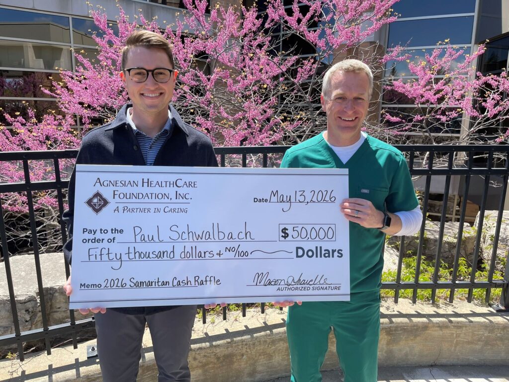 Two men outside holding a big check