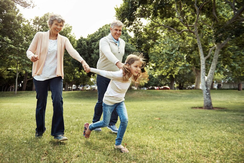 A young child running while holding the hands of grandparents
