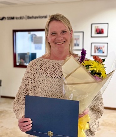 A woman smiling holding flowers and a certificate