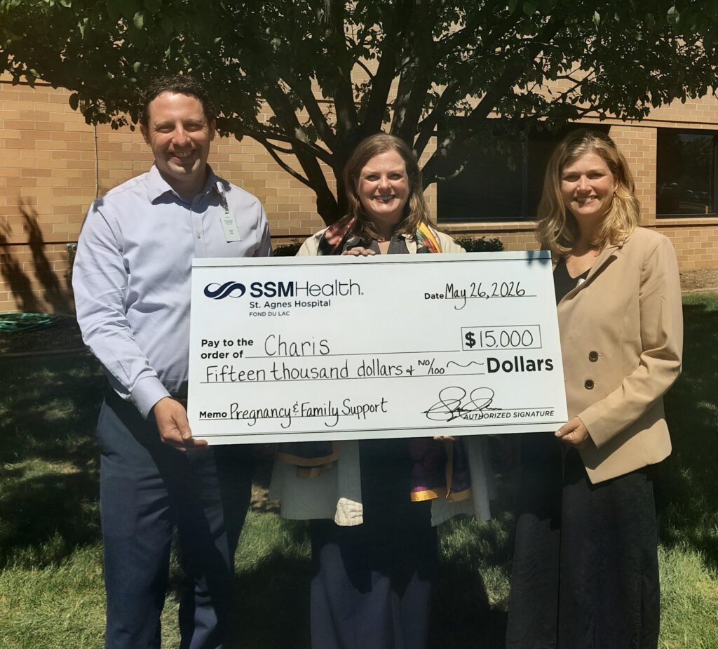 Three people standing outside with a big check