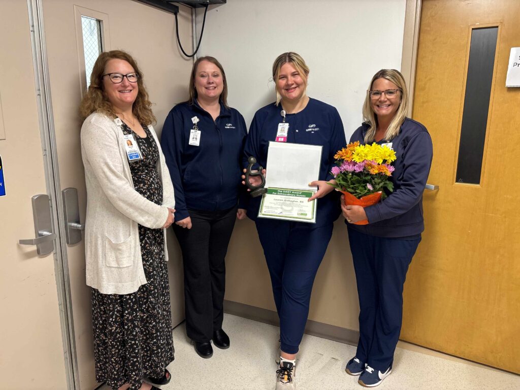 Four women in a hospital hallway with a certificate