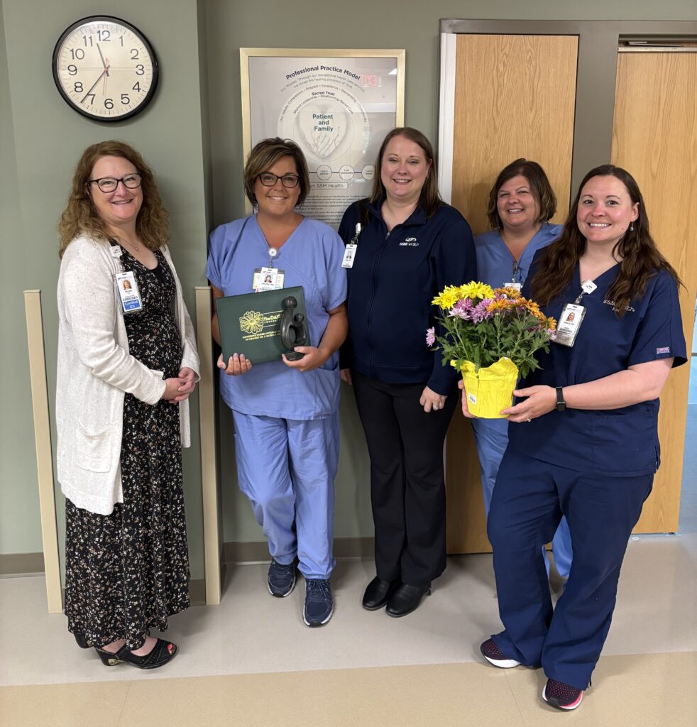 Five women in a hospital hallway with flowers