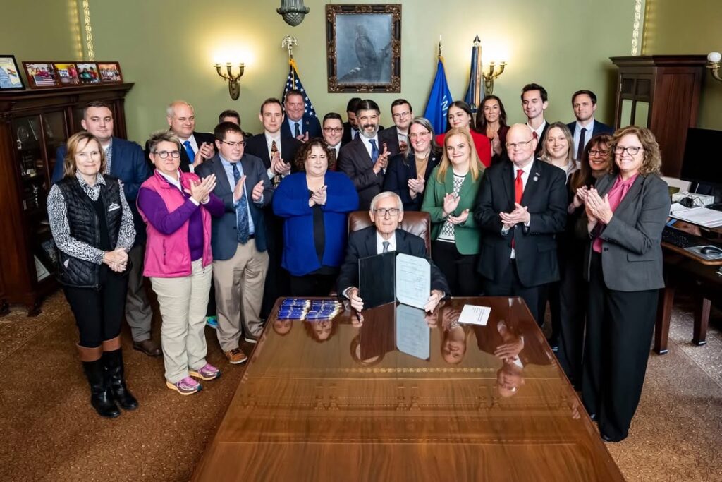 A large group of people in an office with a man at a desk