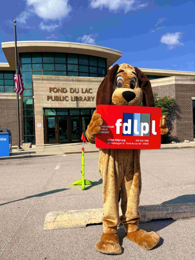 A dog standing in front of the library with a big library card