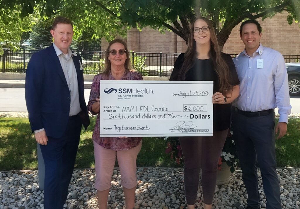 Four people standing outside with a big check