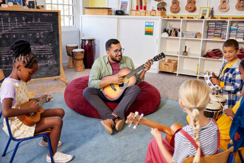 A man playing guitar teaching children