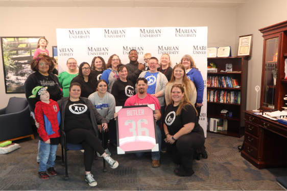 A large group of people inside around a pink football jersey